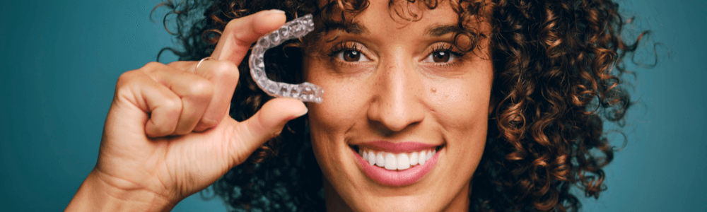 Woman holding clear Invisalign aligners next to face in Wolverhampton dental practice